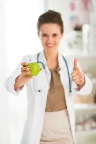 Médica feminina dando maçã verde e mostrando os polegares para cima. Fechar. — Fotografia de Stock